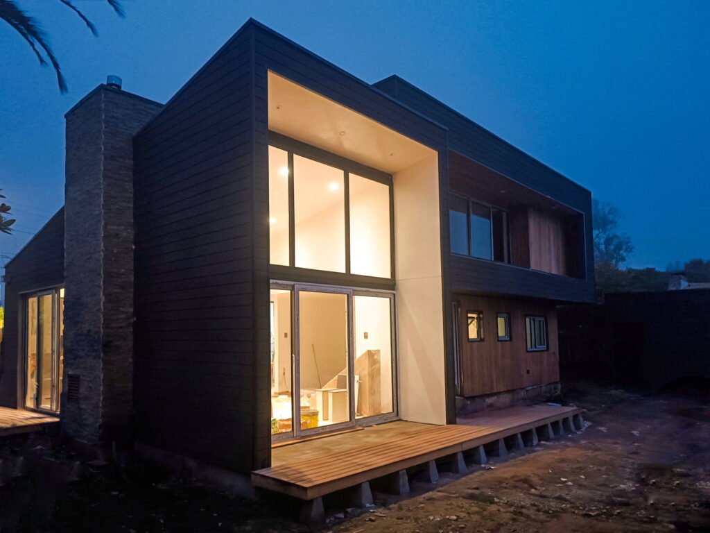 Foto nocturna Casa moderna de madera natural negra con iluminación y salida a terraza.